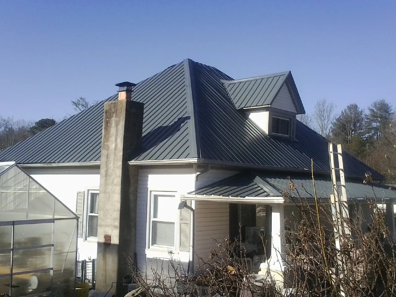 Dark blue standing seam metal roof on a white farmhouse with dormer — Slate & Tile Roof Repair by Roofing Brothers in Gracewood