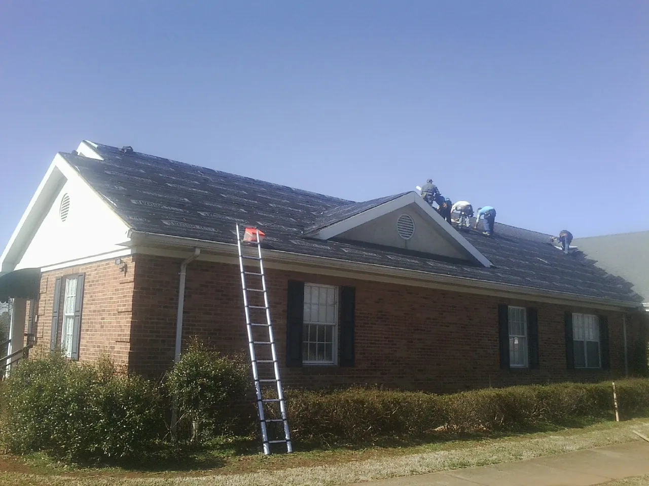 Crew tearing shingles off a brick ranch roof with a ladder set — Emergency Roof Repair work by our crew in Gracewood
