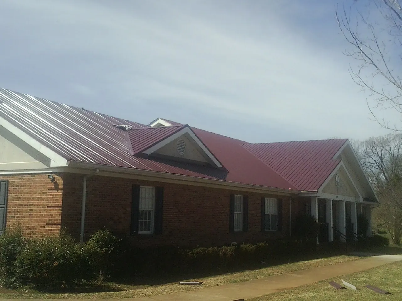 Red metal roof with gabled entries on a long brick building, from a Hail Damage Roof Repair job in Gracewood