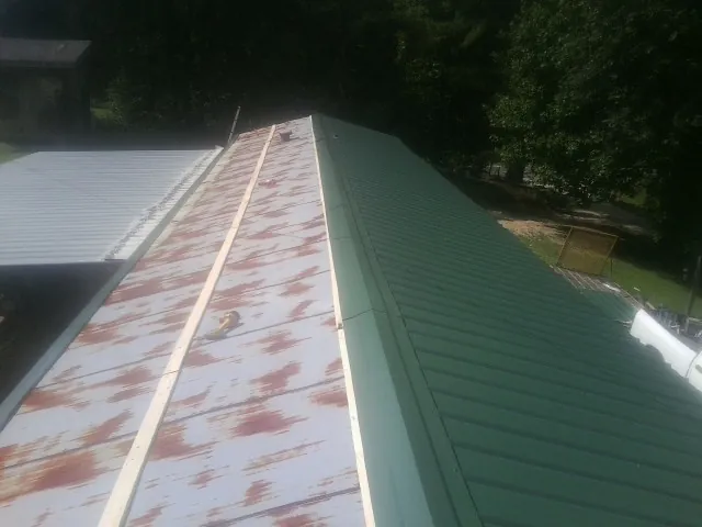 Old rusted panels beside newly installed green metal roofing — Wind Damage Roof Repair by Roofing Brothers in Gracewood