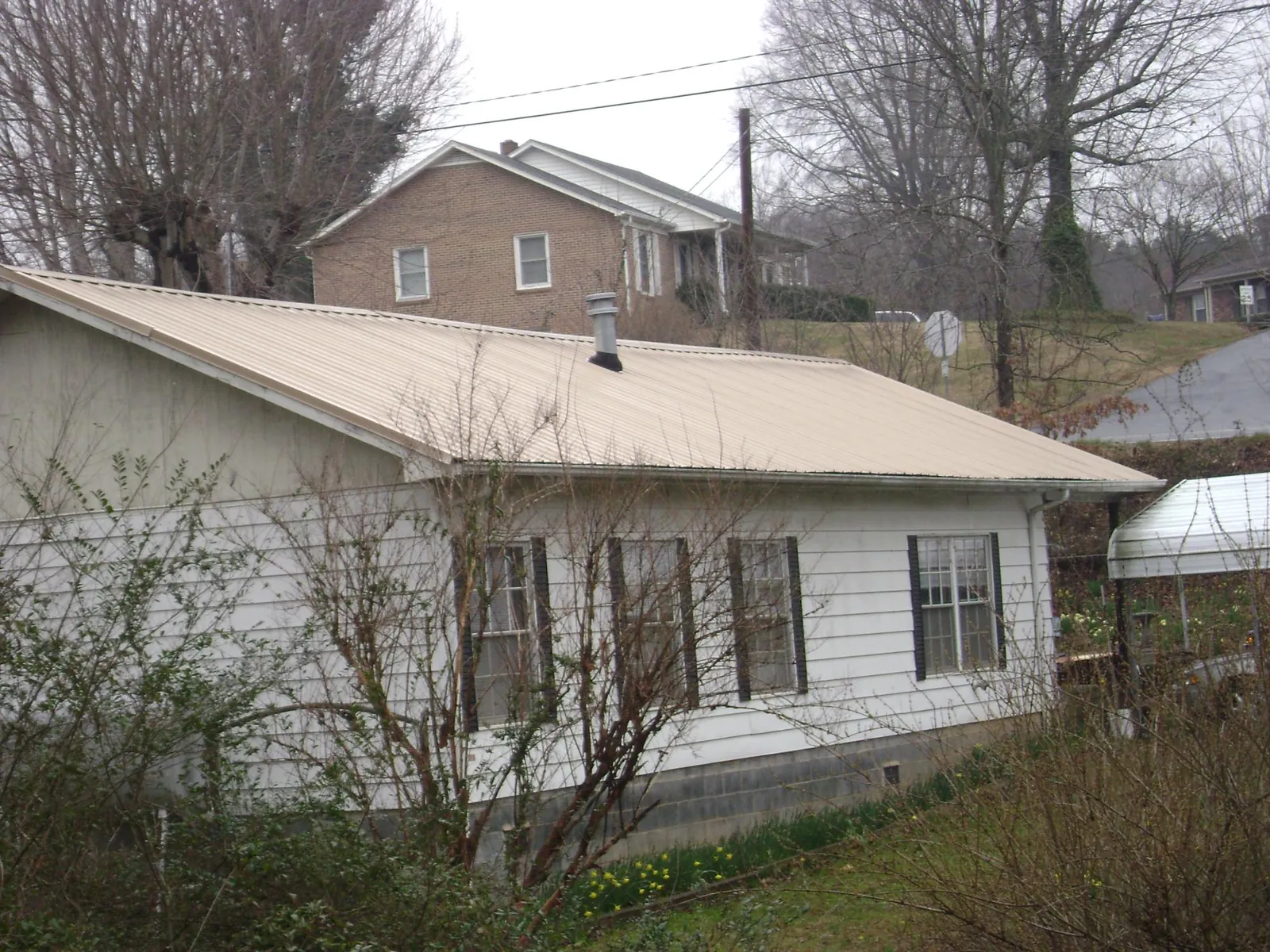 Tan metal roof on a white sided house set into a hillside — Commercial Roofing by Roofing Brothers in Gracewood