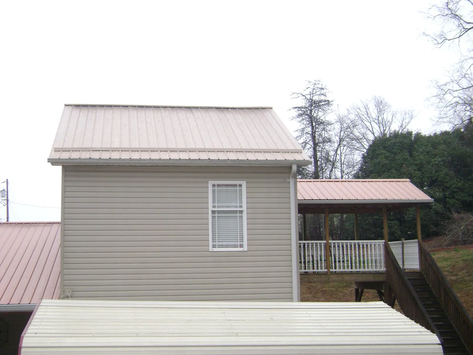Tan metal roofs on a two story addition and attached porch, from a Roof Replacement job in Gracewood